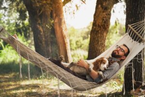 Man sleeping with dog on hammock under trees
