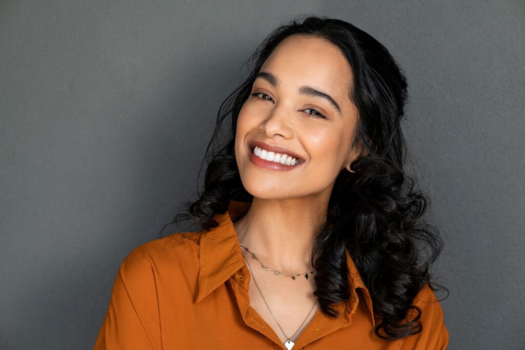 Woman in orange shirt smiling in front of gray background